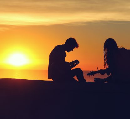 Boy and a girl playing guitar at sunset.